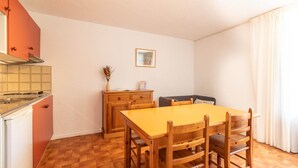 A compact kitchen with a stove, cabinets, and a dining area with a table and chairs. - Peaceful Alpine Triplex Escape (Guillaumes)
