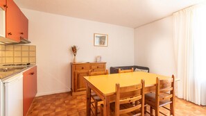 A compact kitchen with a stove, cabinets, and a dining area with a table and chairs. - Peaceful Alpine Triplex Escape (Guillaumes)