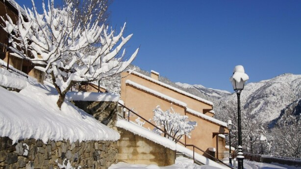 A snow-covered building with a stone wall, a staircase, and a street lamp. - Peaceful Alpine Triplex Escape (Guillaumes)