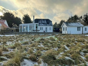 A house with a glass conservatory, a wooden fence, and a grassy field.