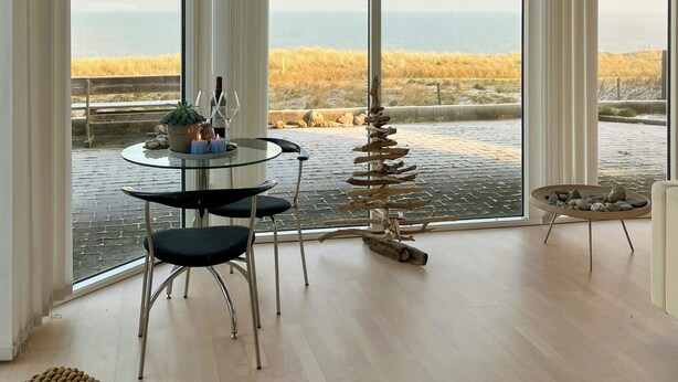 A spacious room with large windows, a round glass table, and a view of a coastal landscape. - Restored fisherman's house on cliff in Thy (Hanstholm)