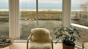 A room with a large window overlooking a beach, a chair, and a potted plant. - Restored fisherman's house on cliff in Thy (Hanstholm)