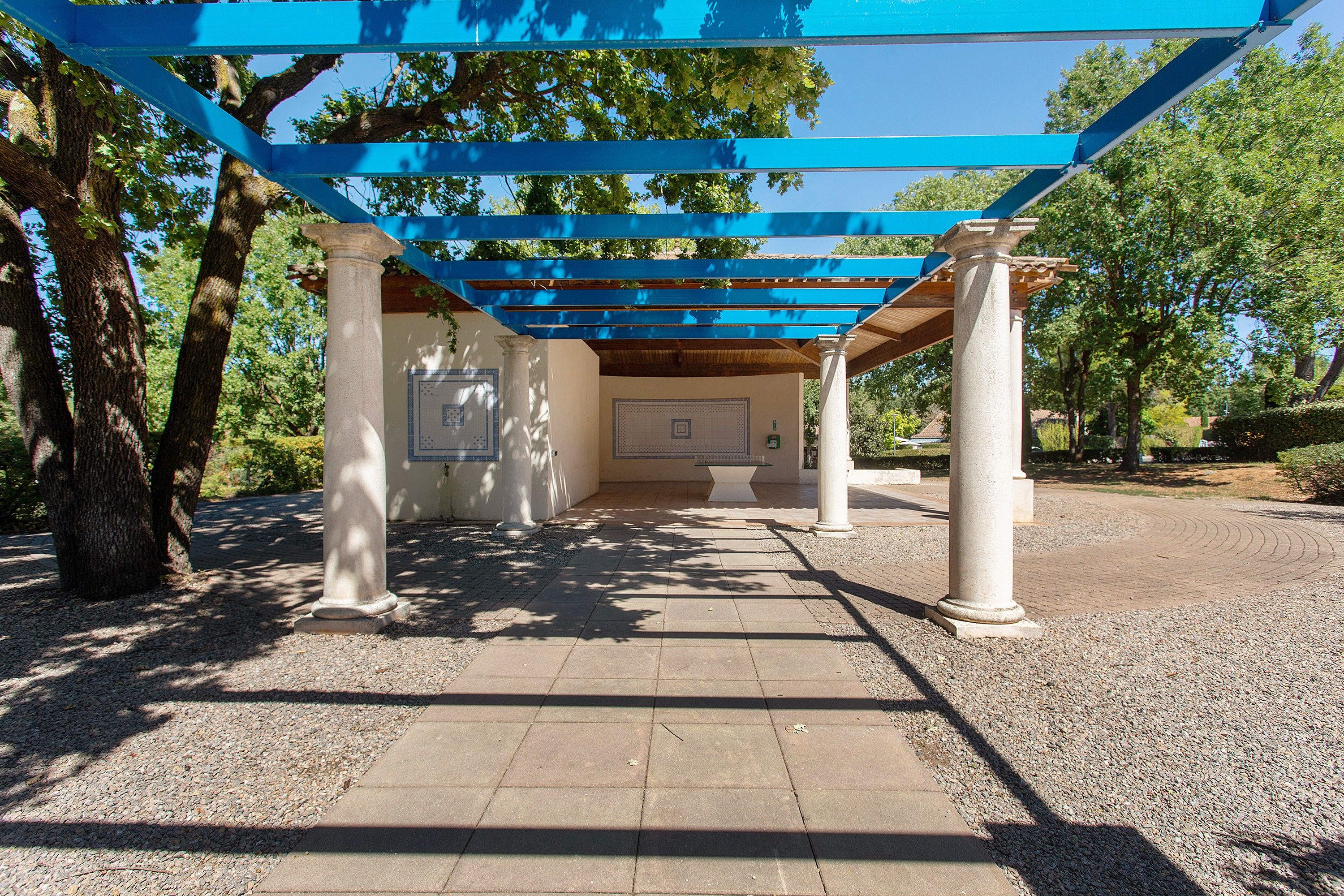 A covered outdoor area with columns and a tiled floor, surrounded by trees.