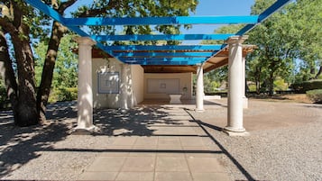 A covered outdoor area with columns and a tiled floor, surrounded by trees.