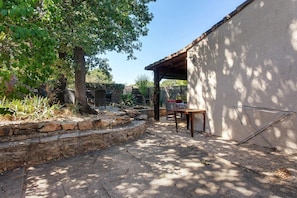 Un espace patio agrémenté d’un escalier en pierre, d’une table et de chaises, le tout entouré de verdure et d’arbres.