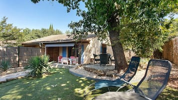 Un patio trasero con mobiliario exterior y un árbol que da sombra.