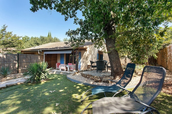 A backyard with a patio, outdoor furniture, and a tree providing shade.