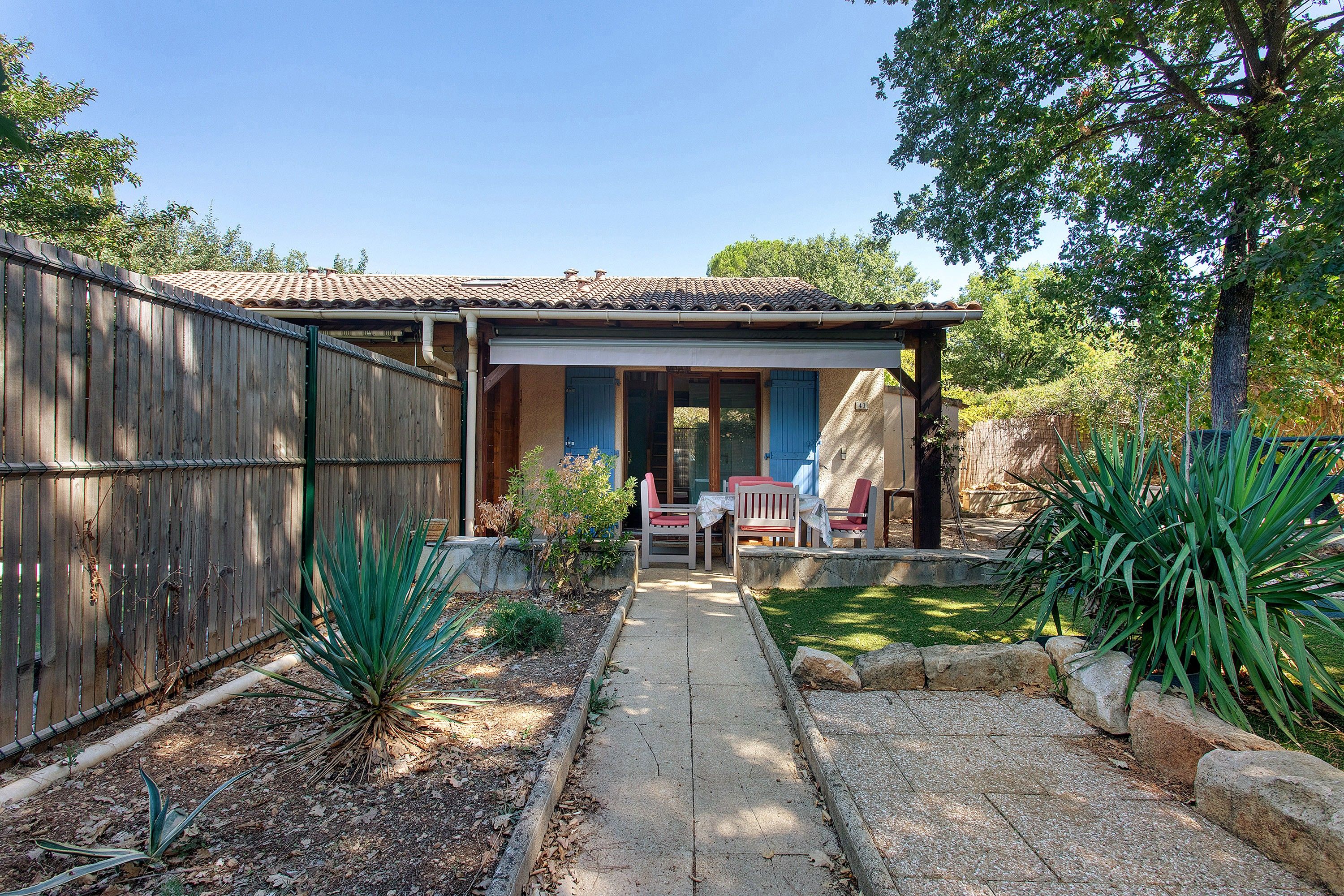 A house with a covered patio, a wooden fence, and a garden with plants and a pathway.