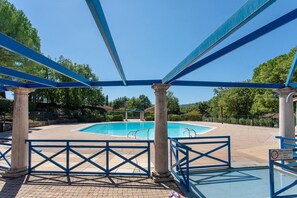 A swimming pool with a blue roof structure and columns, surrounded by a brick walkway.