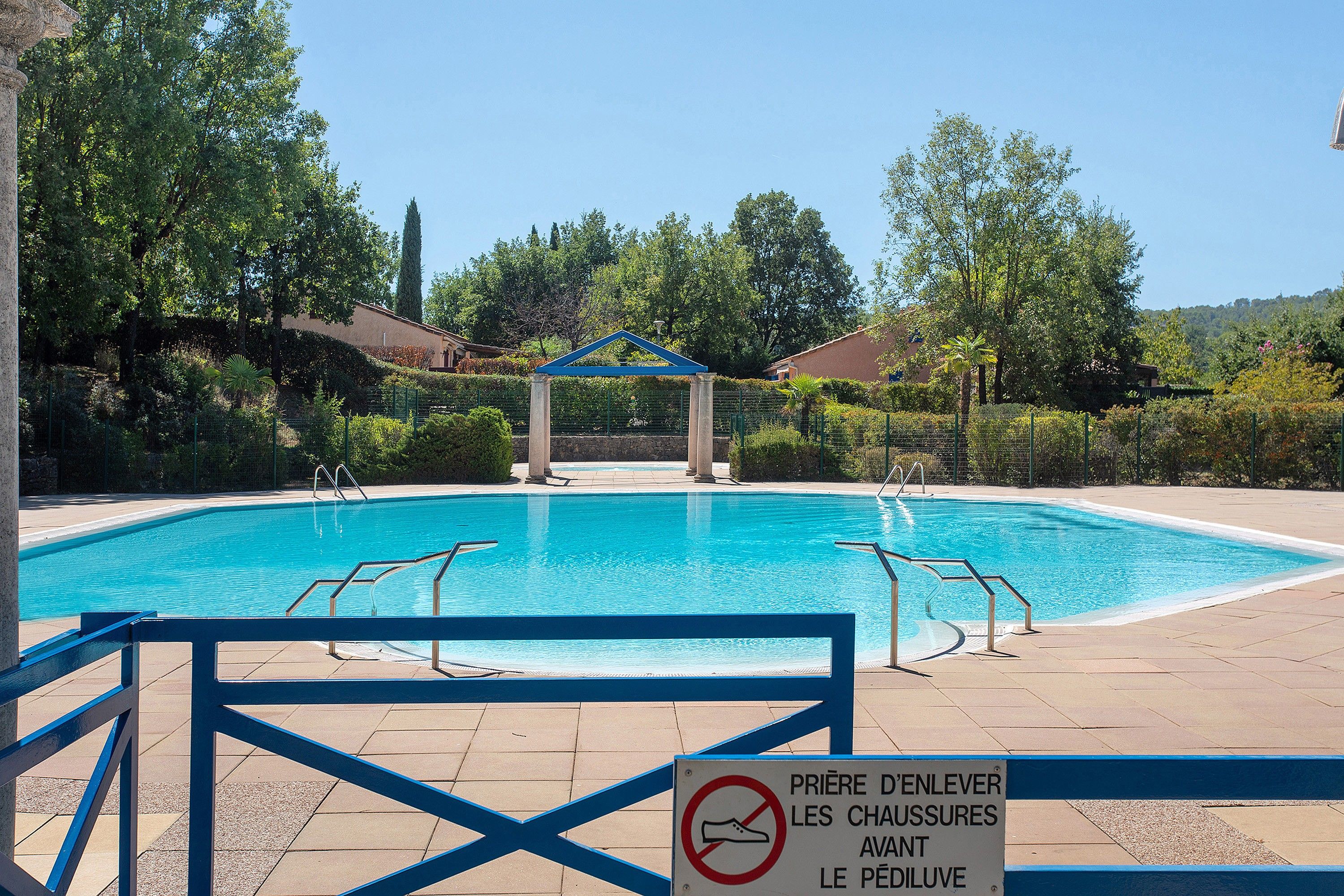 Una piscina con borde azul, rodeada de follaje y un cielo despejado.