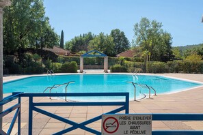 A swimming pool with a blue border, surrounded by greenery and a clear sky.