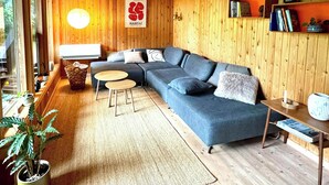 A wooden interior with a sofa, a small table, a lamp, and a bookshelf. - Architectural cottage on 7000 sqm nature plot (Hadsund)