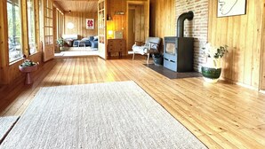 A wooden cabin interior with a fireplace, large windows, and a cozy seating area. - Architectural cottage on 7000 sqm nature plot (Hadsund)