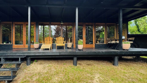 A covered outdoor deck with wooden chairs and potted plants. - Architectural cottage on 7000 sqm nature plot (Hadsund)