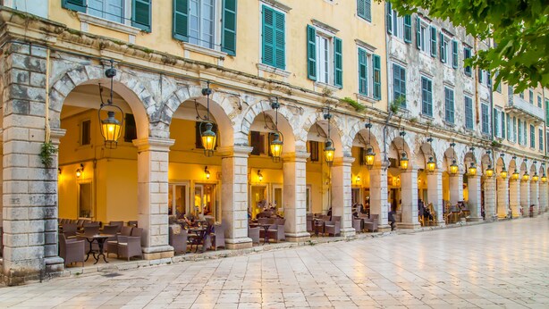 A building with a row of outdoor seating under arches, a tiled floor, and multiple windows with shutters. - Koryfo Old Town Stay by Corfuescapes (Kerkira)