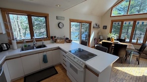 Una cocina con una isla central, un fregadero y una estufa. Ventanas ofrecen luz natural y vistas a árboles.