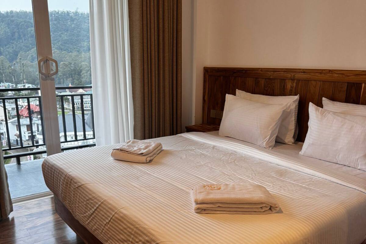 Una habitación de hotel con una cama grande, cabecera de madera y un balcón con vistas.