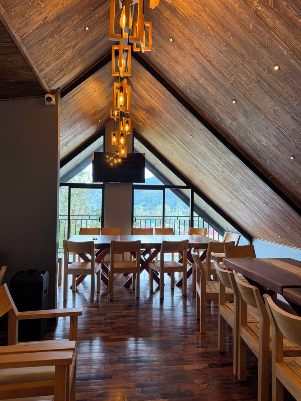 Un espace repas doté d’un plafond haut et de poutres en bois, avec une table centrale entourée de chaises.