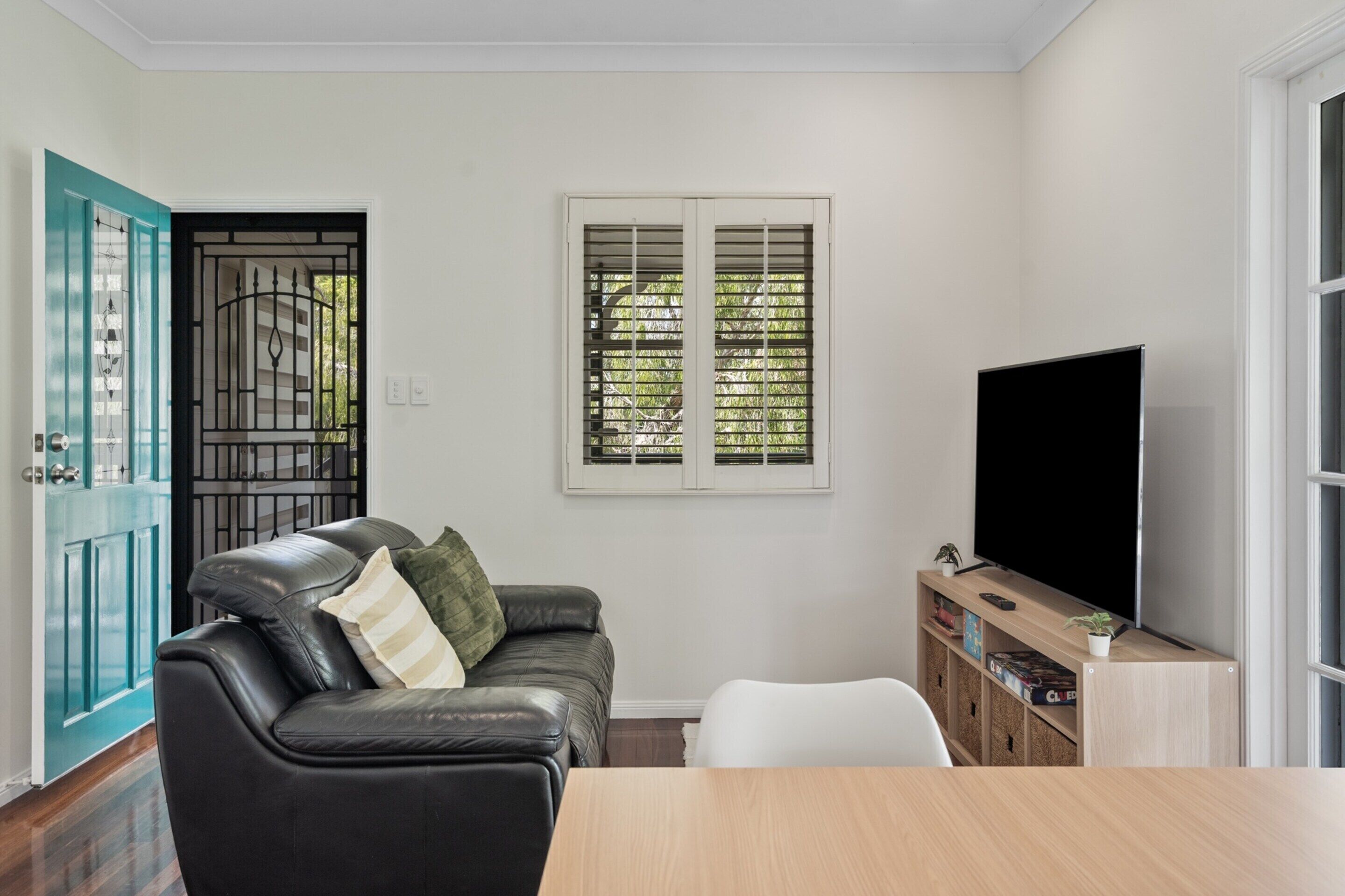 A living room with a black leather sofa, a wooden TV stand, and a window with blinds.