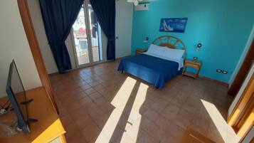 Une chambre à coucher comprenant un lit, un bureau, une chaise, une fenêtre avec des rideaux, un tableau au mur et une vue sur l’extérieur.