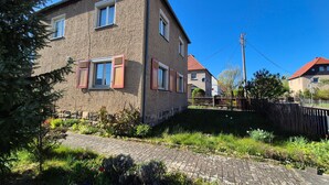 A two-story house with a stone facade, red shutters, and a paved garden area. - Holiday Home 'Elbsandstein vor der Tür' with Private Terrace and Garden (Lohmen)