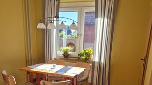 A dining area with a table and chairs, a window with curtains, and a view of the outside. - Holiday Home 'Elbsandstein vor der Tür' with Private Terrace and Garden (Lohmen)