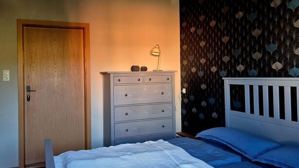 A bedroom with a bed, dresser, and a wall with a patterned wallpaper. - Holiday Home 'Elbsandstein vor der Tür' with Private Terrace and Garden (Lohmen)