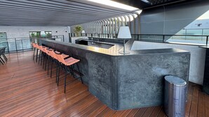 A modern bar area with a counter, stools, and a trash bin. - Flat beira-mar Cabo Branco com rooftop AH215 (João Pessoa)