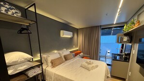 Ein Hotelzimmer mit Bett, einer kleinen Küchenzeile, einem Balkon mit Blick und einem Pflanzenregal.