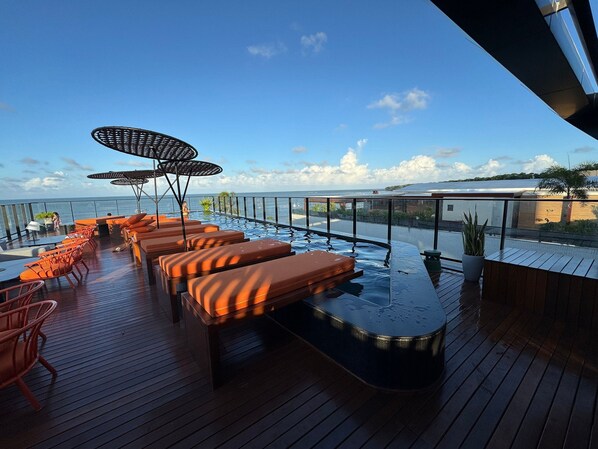Eine Terrasse mit Liegestühlen und einem Whirlpool mit Blick auf ein Gewässer.