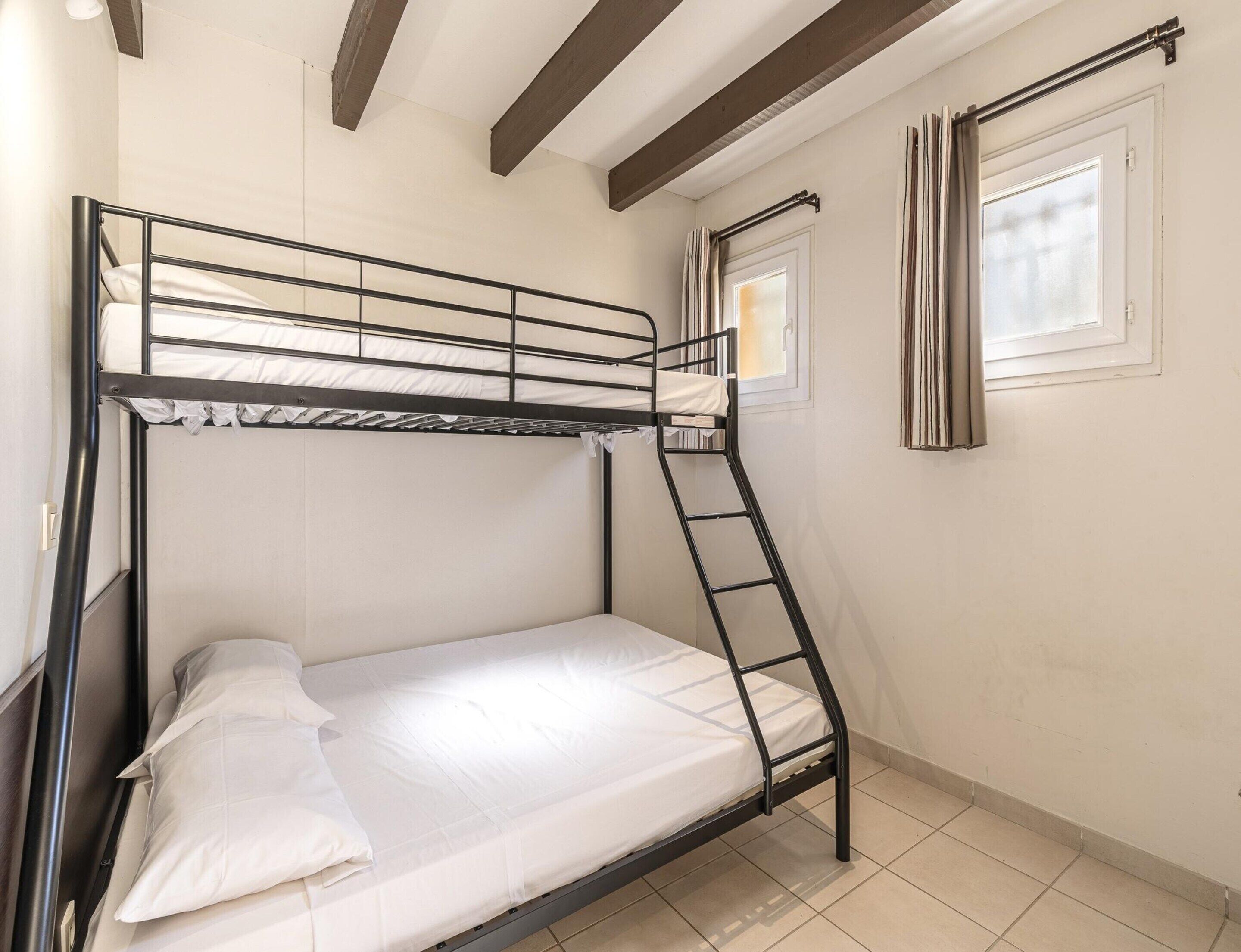 A bunk bed with a ladder, a window with curtains, and a door with a curtain rod.