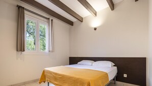 Ein Schlafzimmer mit Bett, einem fenster mit Vorhängen, einer Decke mit freiliegenden Balken und einer wandmontierten Lampe.