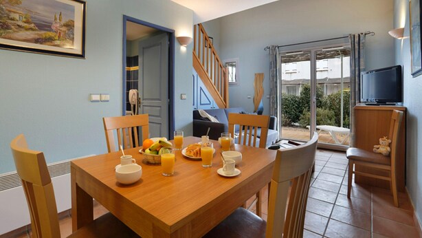 A dining area with a wooden table, chairs, and breakfast items. There is a staircase leading to another room, a television on a stand, and a view through a glass door. - Holiday Home Near Lake Saint-cassien (Tourrettes)