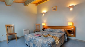A bedroom with a bed, two chairs, a nightstand with a lamp, and a wall-mounted light fixture. - Holiday Home Near Lake Saint-cassien (Tourrettes)
