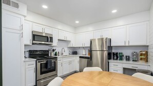 A modern kitchen with white cabinets, stainless steel appliances, a wooden dining table, and a built-in dishwasher. - 2 Mins to ASU, Swimming Pool, King Bed (Tempe)