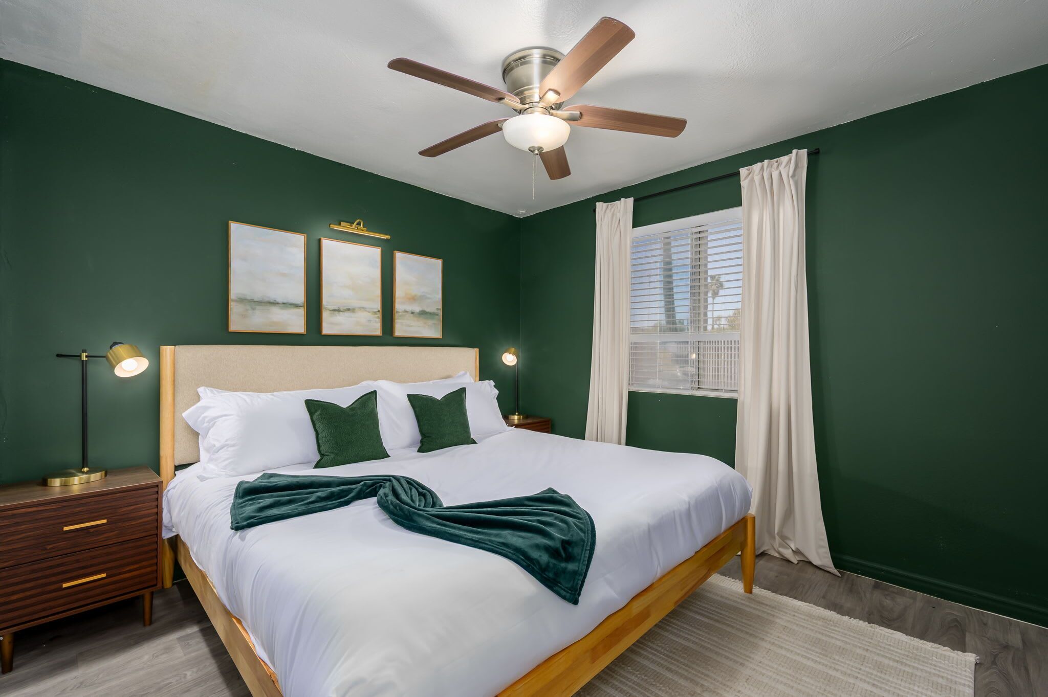 Ein Schlafzimmer mit Bett, Deckenventilator, Nachttisch, Lampe und einem Fenster mit Vorhängen.