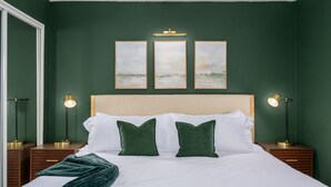A neatly made bed with white linens and green pillows, flanked by two bedside tables with lamps, in a room with dark green walls and a ceiling light fixture. - 2 Mins to ASU, Swimming Pool, King Bed (Tempe)