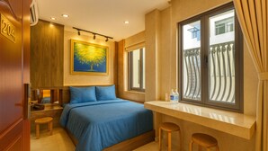 Ein Hotelzimmer mit Bett, einem Gemälde, einem Fenster mit Vorhängen und einem kleinen Tisch mit Hockern.