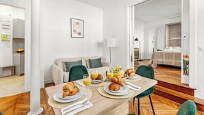 Ein moderner, gut beleuchteter Raum mit Esstisch, gedecktem für ein Frühstück, einer Couch und einem Bett im Hintergrund.
