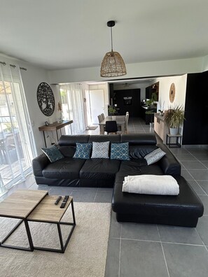 A modern living room with a black sectional sofa, a wooden coffee table, and a dining area with a table and chairs. - 🌿Very luminous villa near Uzès - peace & quiet 🌿 (Cavillargues)