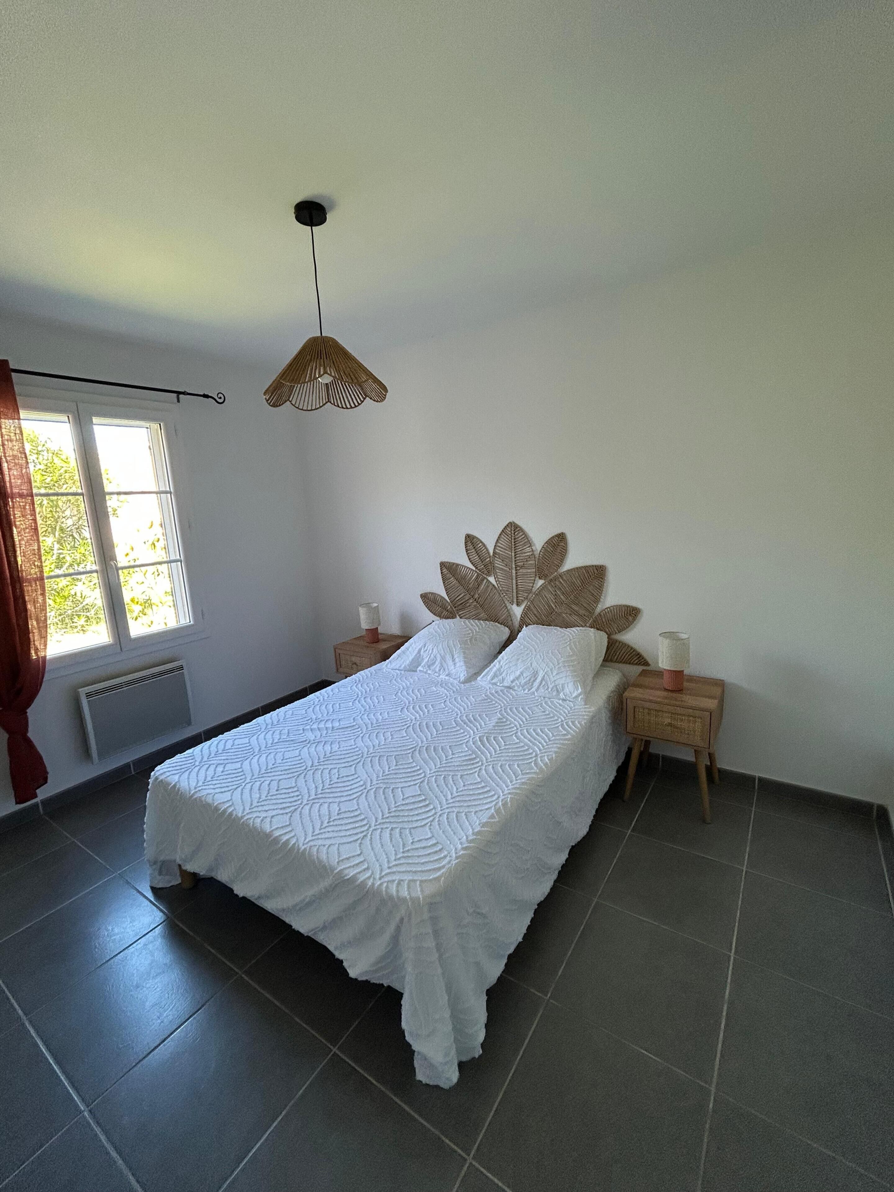Une chambre à coucher avec un lit, une fenêtre, un luminaire suspendu et une table de chevet.