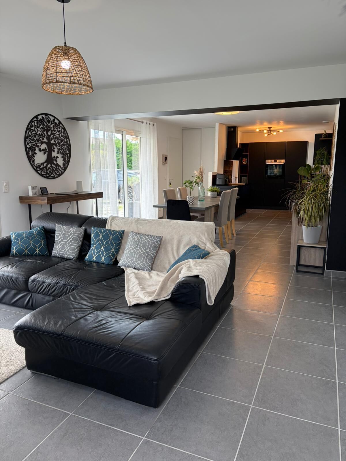 A modern living room with a black leather sofa, a dining table, and a kitchen in the background.