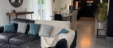A modern living room with a black leather sofa, a dining table, and a kitchen in the background.