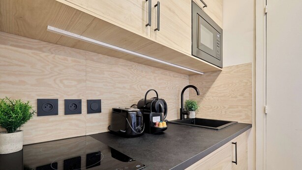 A modern kitchen with wooden cabinets, a black countertop, a built-in microwave, a coffee maker, and a sink. - Charming Suite Center of Paris Le Marais (Paris)