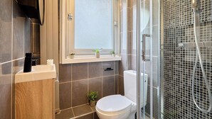 A bathroom with a toilet, a shower enclosure, a window, and a small shelf with toiletries. - Charming Suite Center of Paris Le Marais (Paris)
