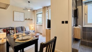 A modern living room with a dining table set for two, a sofa, a TV, and a kitchen area visible through a glass door. - Charming Suite Center of Paris Le Marais (Paris)