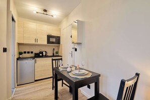 Een kleine keuken met moderne apparaten, een eettafel gedekt voor twee personen en een kleine koelkast.