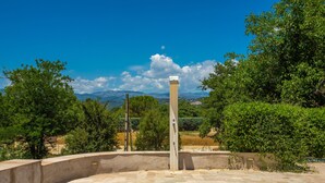 A courtyard with a tall, narrow column, a curved wall, and a view of distant mountains and trees. - Holiday Home 'Lou Mazet Du Gaudon' with Shared Pool, Shared Terrace and Shared Garden (Montauroux)