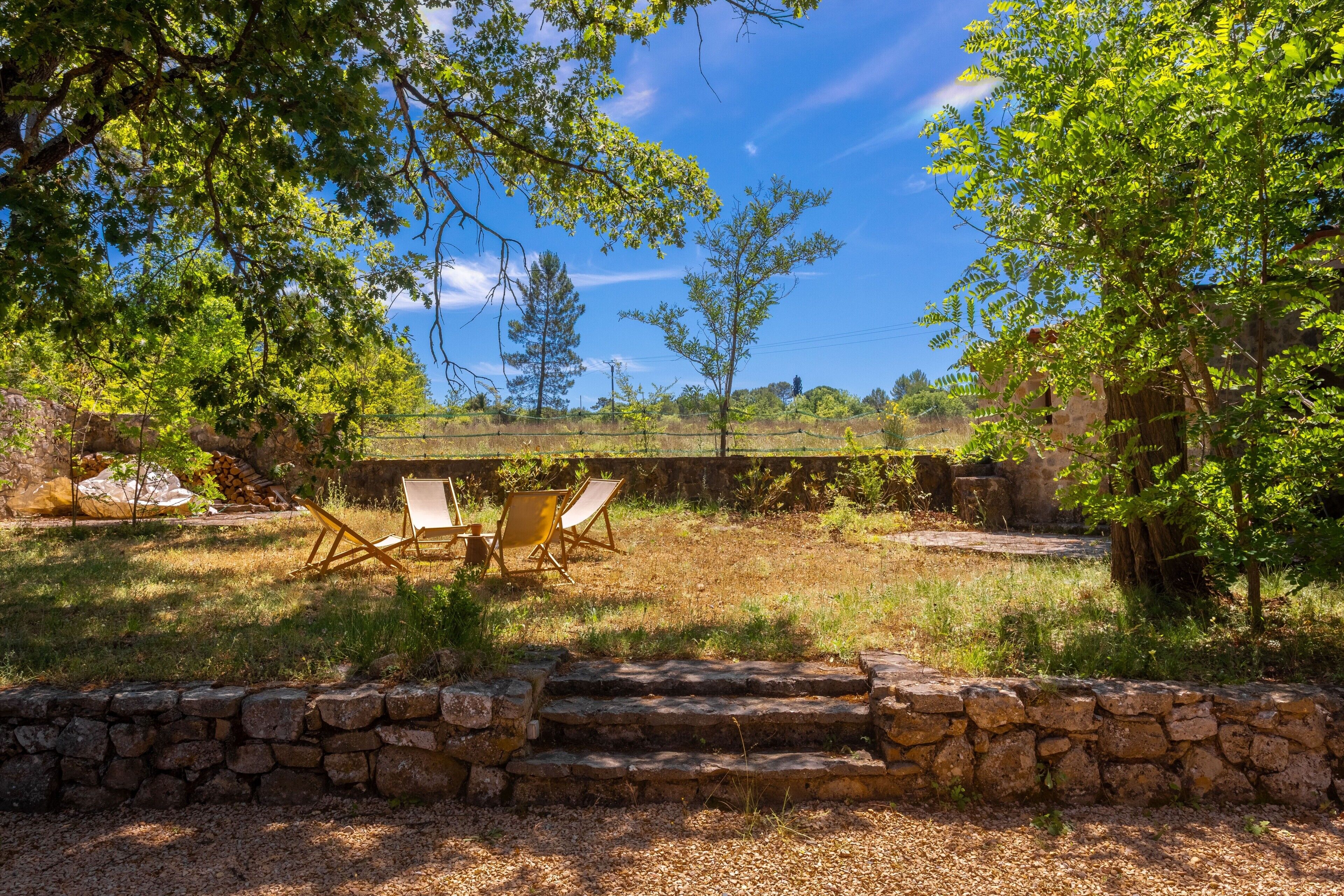 A stone wall, a wooden pergola, and two chairs in a garden.