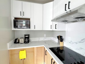 A kitchen with white cabinets, a microwave, a coffee maker, and a stove.
